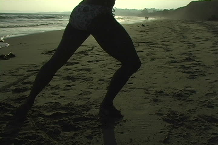 A beautiful, silhouetted young woman performs on the beach.  