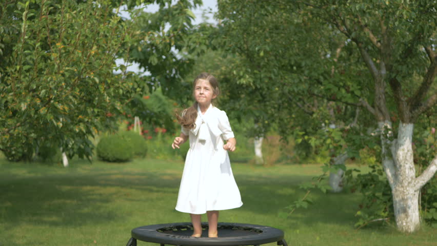 The cute girl jumping on trampoline in the garden