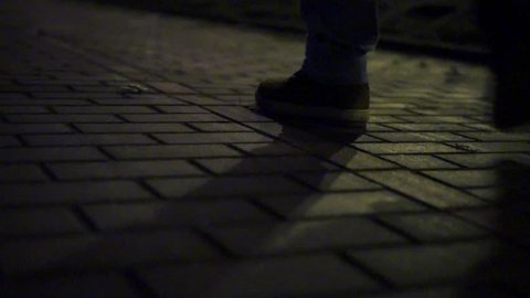 Close up footage of man walking alone in dark ally on brick sidewalk.