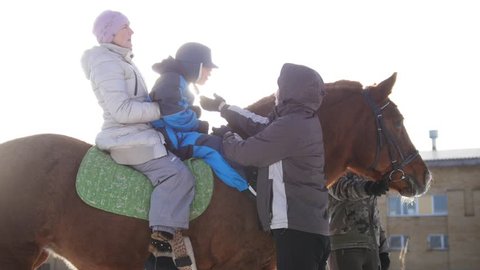 Contact kids therapy and rehabilitation horse-riding club - staff conducts hippotherapy for kid with cerebral palsy syndrome at winter day, over the sun