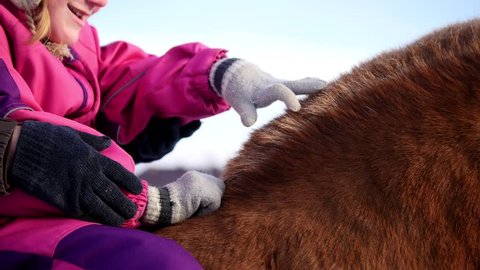 Hippotherapy for kid with cerebral palsy syndrome at winter cold day - contact kids therapy and rehabilitation horse-riding club - young girl and her mother rides on horse, pats horseback, close up