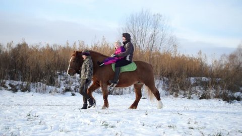 Hippotherapy for kid with cerebral palsy syndrome at winter cold day - contact kids therapy and rehabilitation horse-riding club - young girl and her mother rides on horse