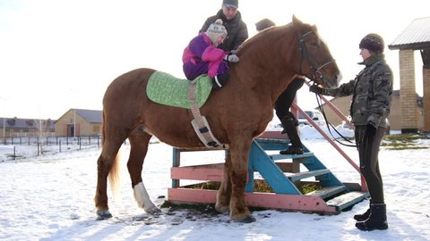 Hippotherapy for kid with cerebral palsy syndrome at winter cold day - contact kids therapy and rehabilitation horse-riding club - young girl and her parents on horse