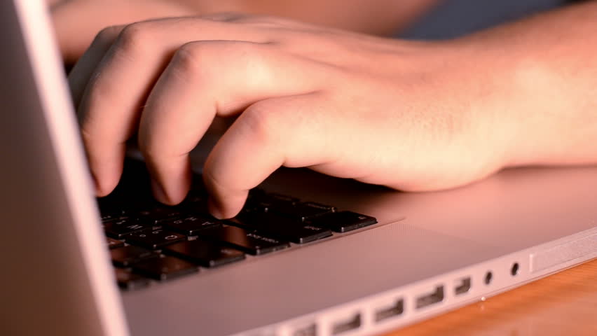 Closeup of the hands of a man typing on a laptop.