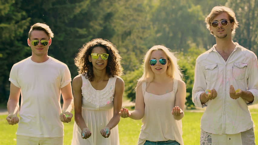 Cheerful young people throwing up colorful powder and hugging at summer party