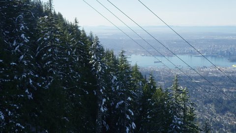 A view from the Grouse Mountain gondola.  Snowy trees roll by with the Vancouver skyline and ocean far below. 4k.

