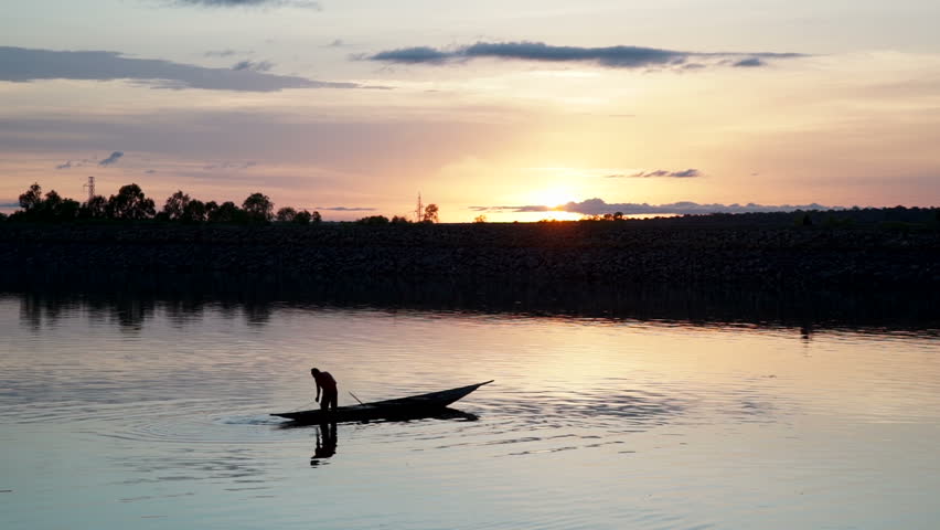 Silohuette, Sunset in the background of a fisherman fishing with a small canoe on a lake at sunset in Mali, Africa.