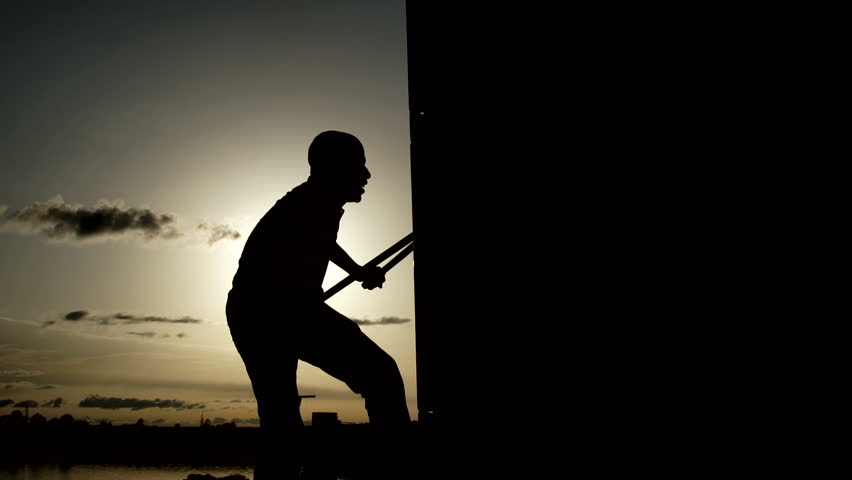 Silohuette of a man opening a container with tongs. Sunset in the background.
