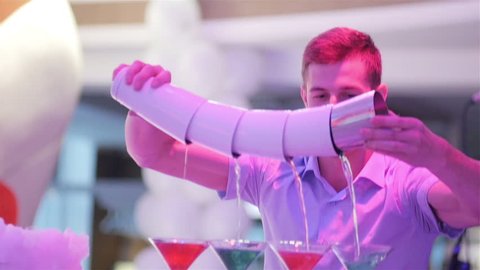 Flair bartending. Barman shows trick. Smiling bartender pours shaken alcoholic cocktail to colorful martini glasses using special technique of making many cocktails the same time from shaker tin chain