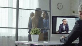 Office worker having conversation with director via webcam while female colleague joining their video conference