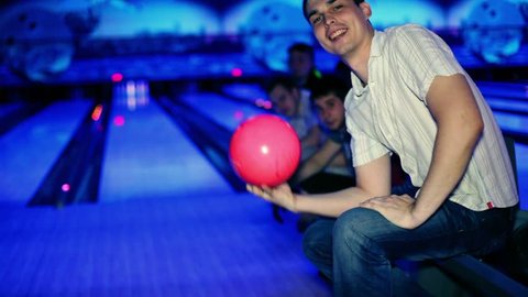 Young man holds pink bowling ball and then throws it, his friends support him