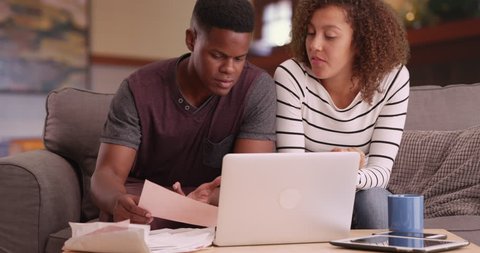 Black millennial couple paying bills with laptop computer in living room. African American man and woman planning investments online in their house. 4k.