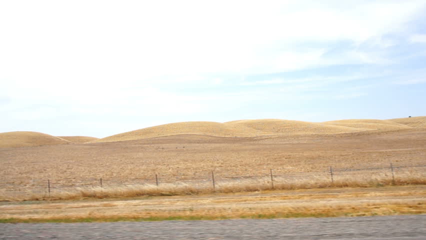 Tracking view driving down a highway past dusty, rolling yellow plains. | Shutterstock HD Video #21856516