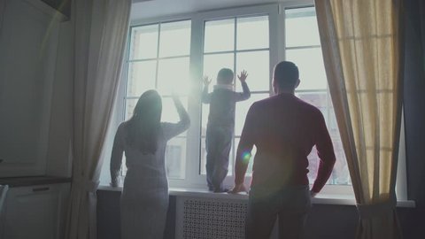 Happy family with the child's back window. Family silhouette in the window. Parents and child looking out the window, the sunlight in the window. The concept of parental care of the child and family.