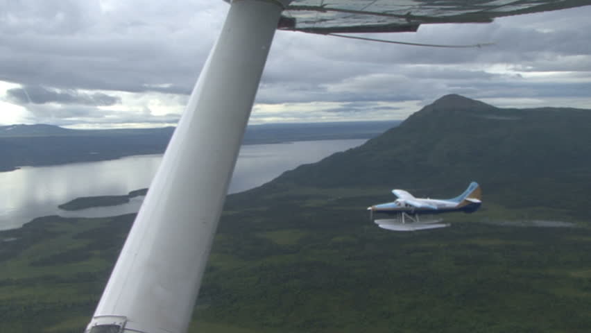 A float plane is seen in the distance from under wing of our plane as it flies