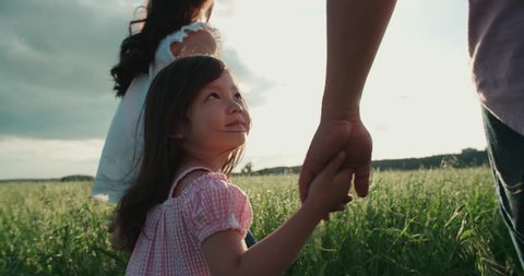 little Asian girl walking on the green field with their parents, holding the hand of his father, slow motion