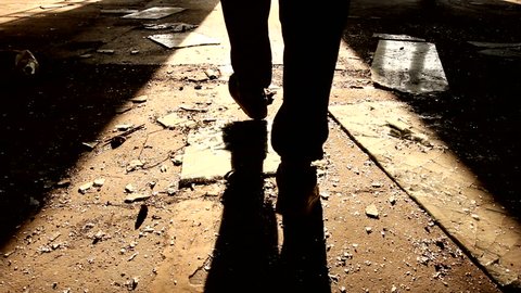 Murderer walks away, leaving the crime scene in some old ,dark,messy building. Shadows are visible, high contrast made of sunlight falling through opened door.