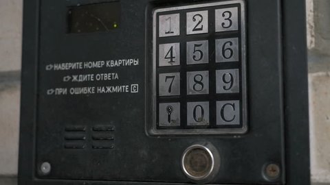 Person pushing the buttons on the panel of the intercom outdoors. Text on the control panel Dial the number of the apartment. Wait for a response. During the error push the C