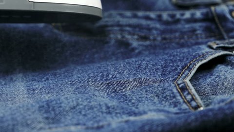 Woman steaming the denim fabric on the ironing table indoors. Close up