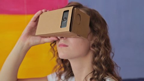 Young curly woman using Virtual Reality Glasses. Virtual reality mask. VR. Google cardboard. Colorful background. Future and technology concept Video de stock