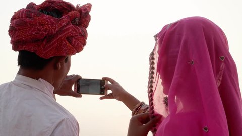 Indian couple looking back at the camera and taking photos of sunset at holy Pushkar lake, Rajasthan 