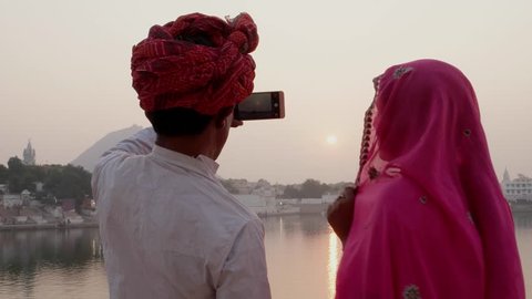 Pan away from Indian couple in traditional  dress taking photos of sunset at holy Pushkar lake, Rajasthan 