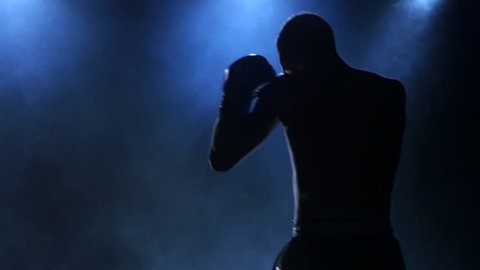 Boxer shows workout before the fight. Silhouette on dark background