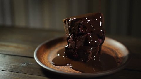 Dark chocolate flowing on brownie cake. Chocolate cake on ceramic plate. Homemade dessert. Chocolate topping on brownie stack.