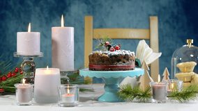 Festive holiday table with English style Christmas fruit cake on glamorous table setting with pink candles and blue background, full table static. 