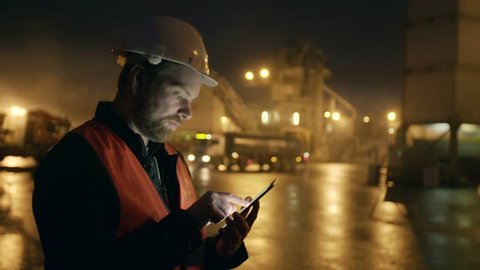 Engineer in hardhat with a tablet computer looks at truck on heavy industry