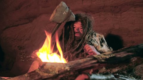 Prehistoric caveman looks at the fire and his spear in his cave