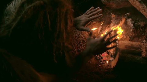 Neanderthal man warms his hands by the first bonfire in his cave