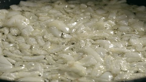 Close-up  -  chopped onion is fried in a frying pan and moved by a wooden spatula