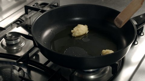 Melted butter in a frying pan. Close-up - female hand moves butter by a wooden spatula. Chopped onion add  into the pan from the bowl. 