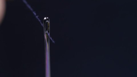 macro close up of male hand putting thread through needle head