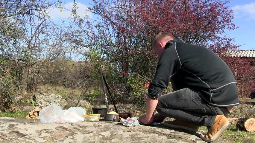 Cooking food outdoors near bonfire. Man cuts meat
