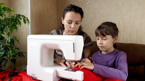 The child learns to sew on the sewing machine. Mom teaches daughter to sew on a typewriter.