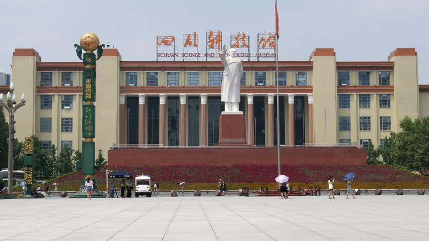 Chengdu Sichuan science & technology museum front, road passing people traffic, police patrol English & Chinese sign, Chairman Mao statue & flag wrapped around flagpole with clear blue sky background.