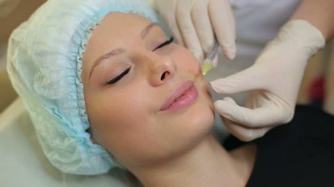 Close-up of hands of cosmetologist making botox injection to female lips. Young woman gets facial injections in salon. Facial rejuvenation.