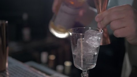 Bartender is making cocktail at bar counter, adding some bitter in the shaker