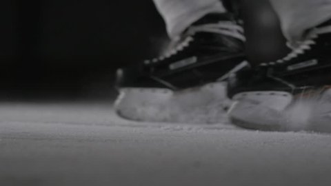 Hockey player make ice sparkles on high speed braking in dark on arena. Motion blur. Legs view only