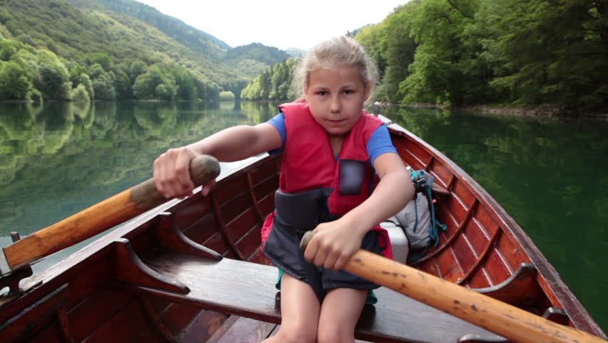 Small girl in red life jacket rowing with paddles in wooden rowboat on surface of Biogradskoe lake in Biogradska Gora national park. Montenegro