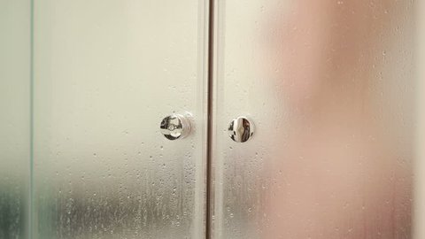 Woman behind blurry glass. Girl preparing take shower. Woman in bathroom