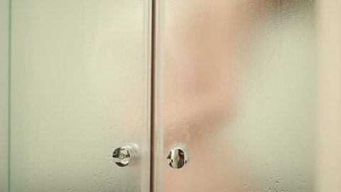 Woman behind blurry glass. Girl preparing take shower. Woman in bathroom