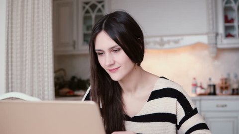 portrait of a beautiful young brunette woman uses laptop in a bright dining.