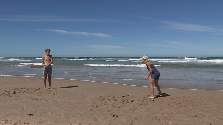 Two teenagers playing cricket on the beach in slow motion 