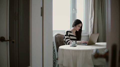 Woman uses laptop and enjoying morning coffee on a bright dining. slider to the left, view through the open doors