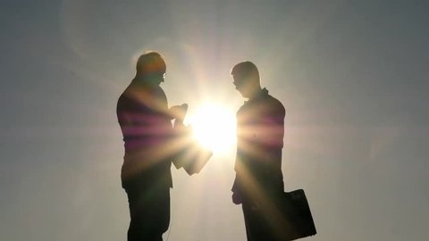 Two men changing cases and shaking hands of each other silhouettes