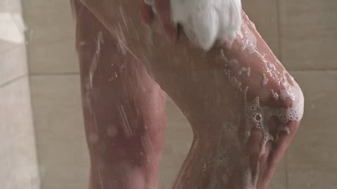 Closeup of woman washing legs with bath buff under shower