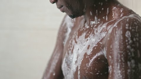 Closeup of African man cleaning his body with foamy bath buff under shower